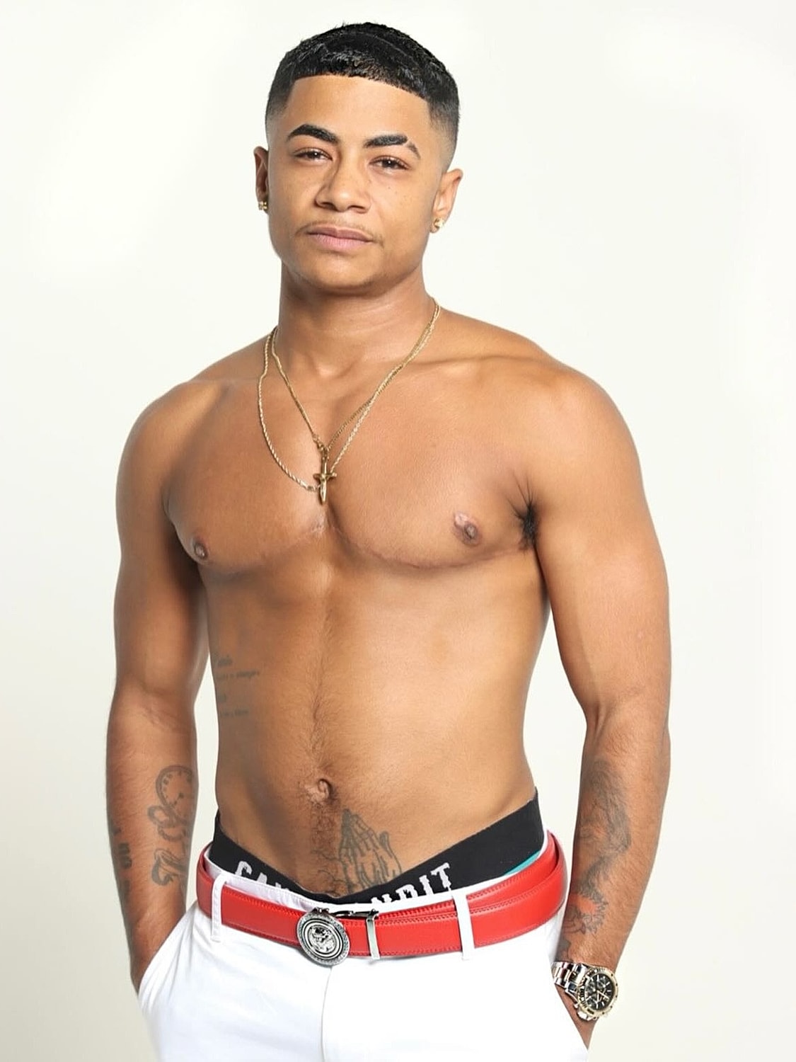 Young man posing shirtless with tattoos and jewelry.