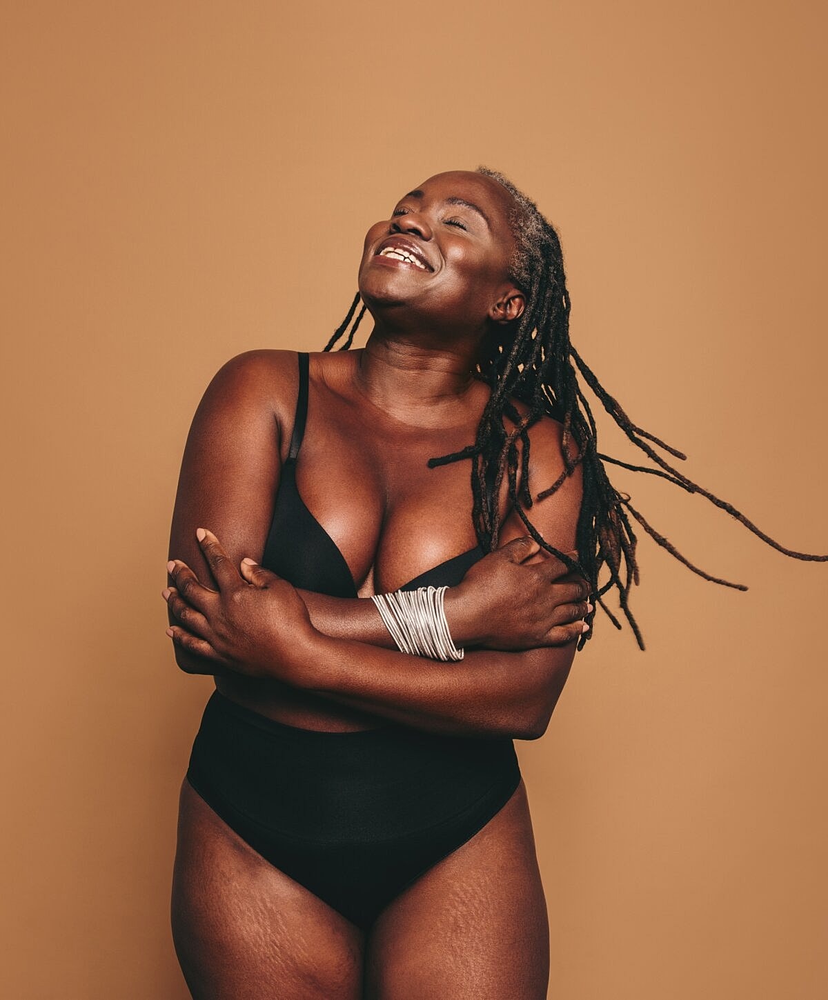 Smiling woman with dreadlocks against a warm backdrop.