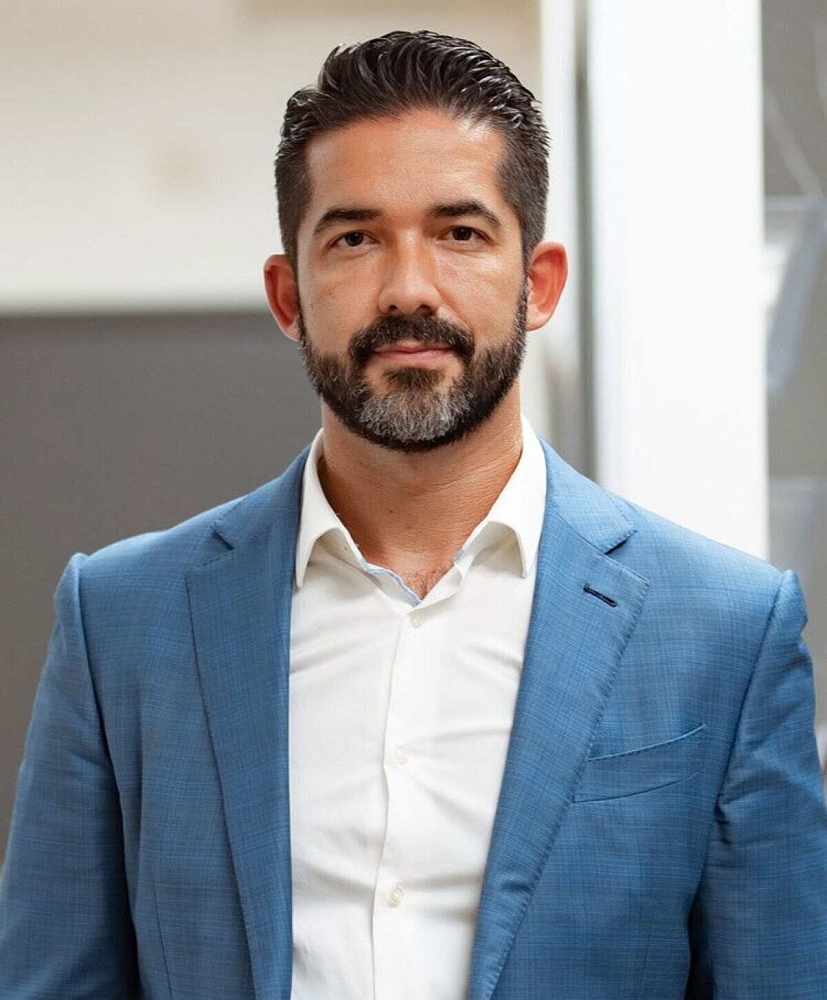 Man in blue suit standing confidently indoors.