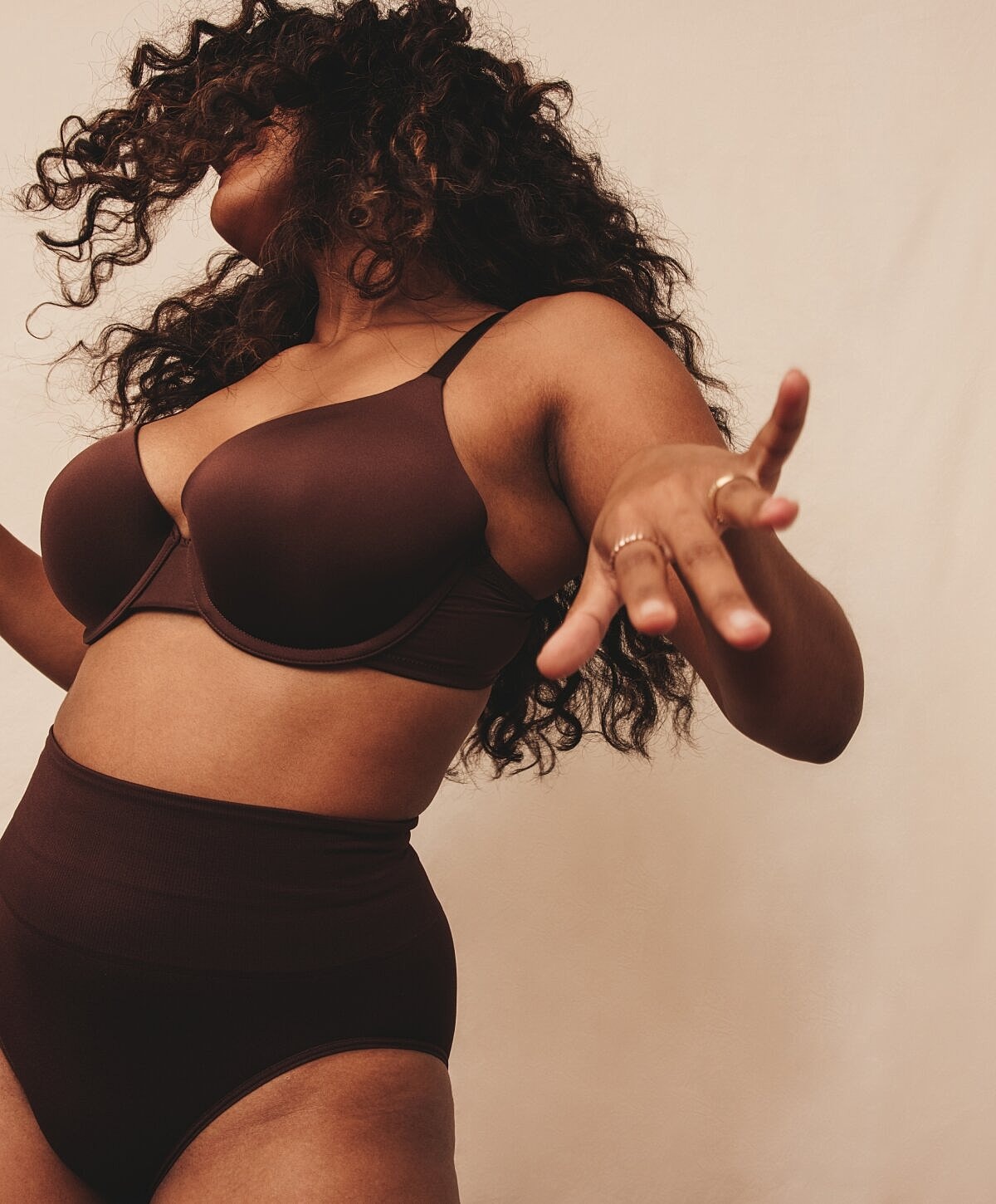 Model posing in brown lingerie against neutral background.