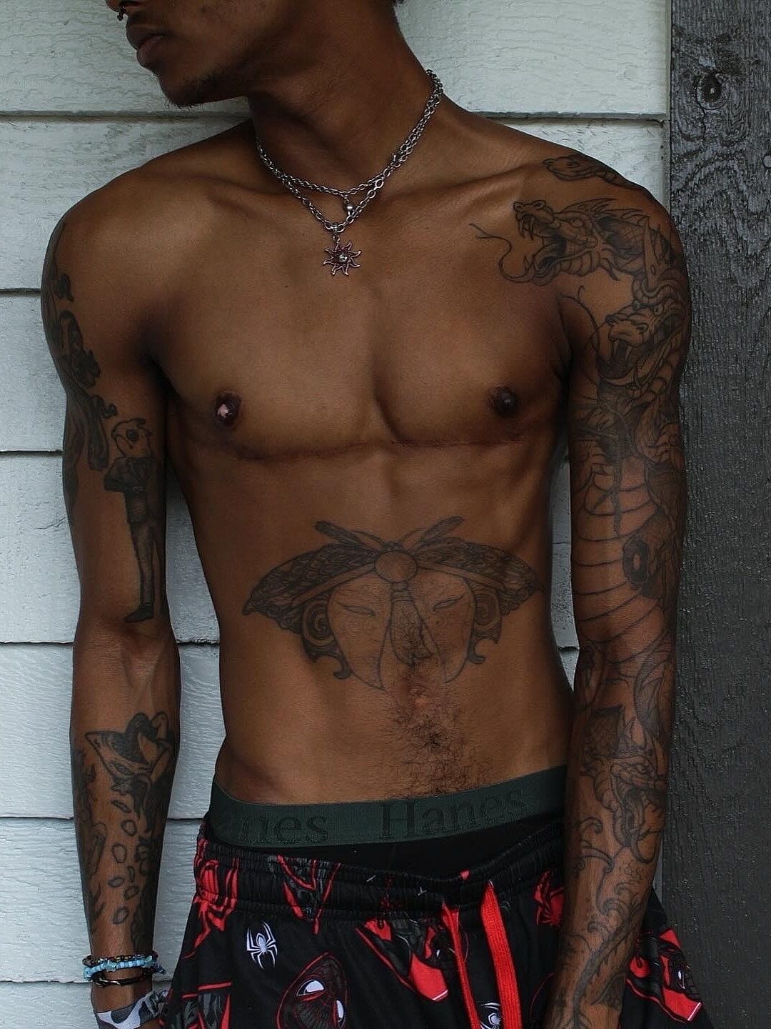 Shirtless person with tattoos and jewelry.