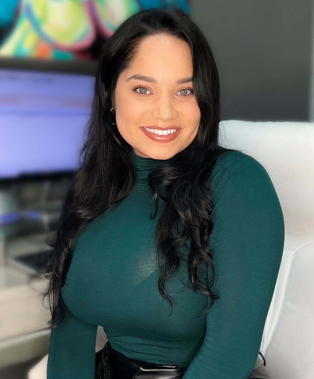 Smiling woman in green top, seated indoors.