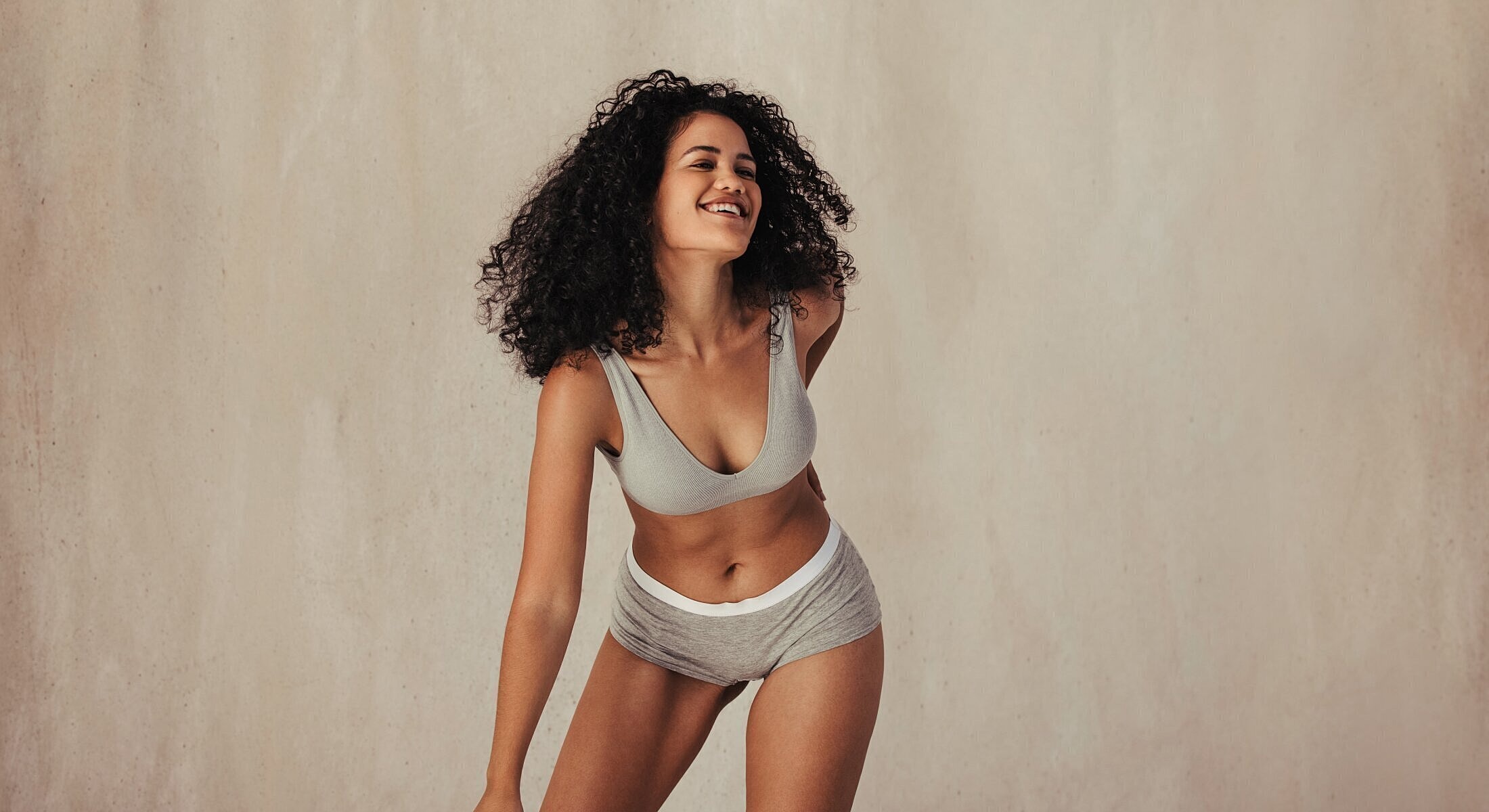 Smiling woman in casual lingerie, beige background.