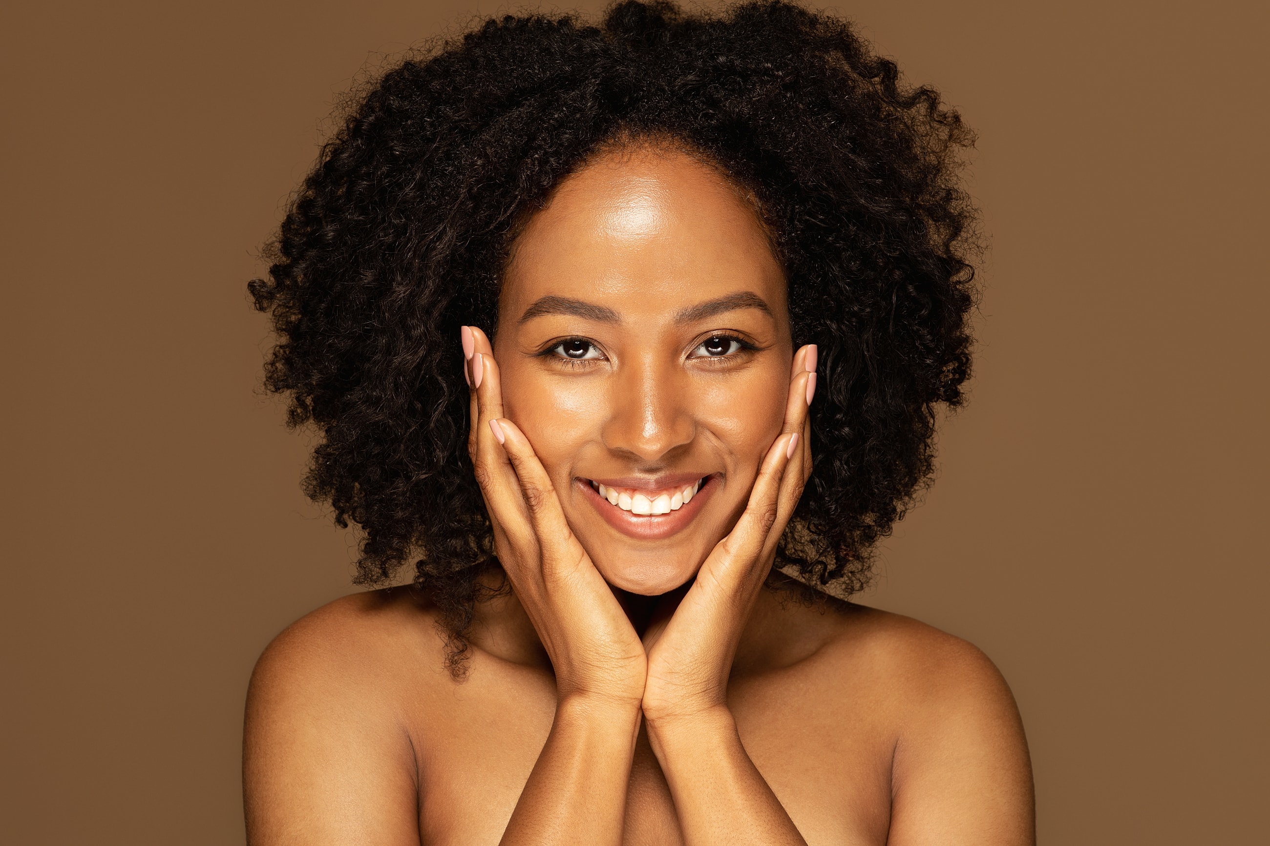 Smiling woman with curly hair on brown background.